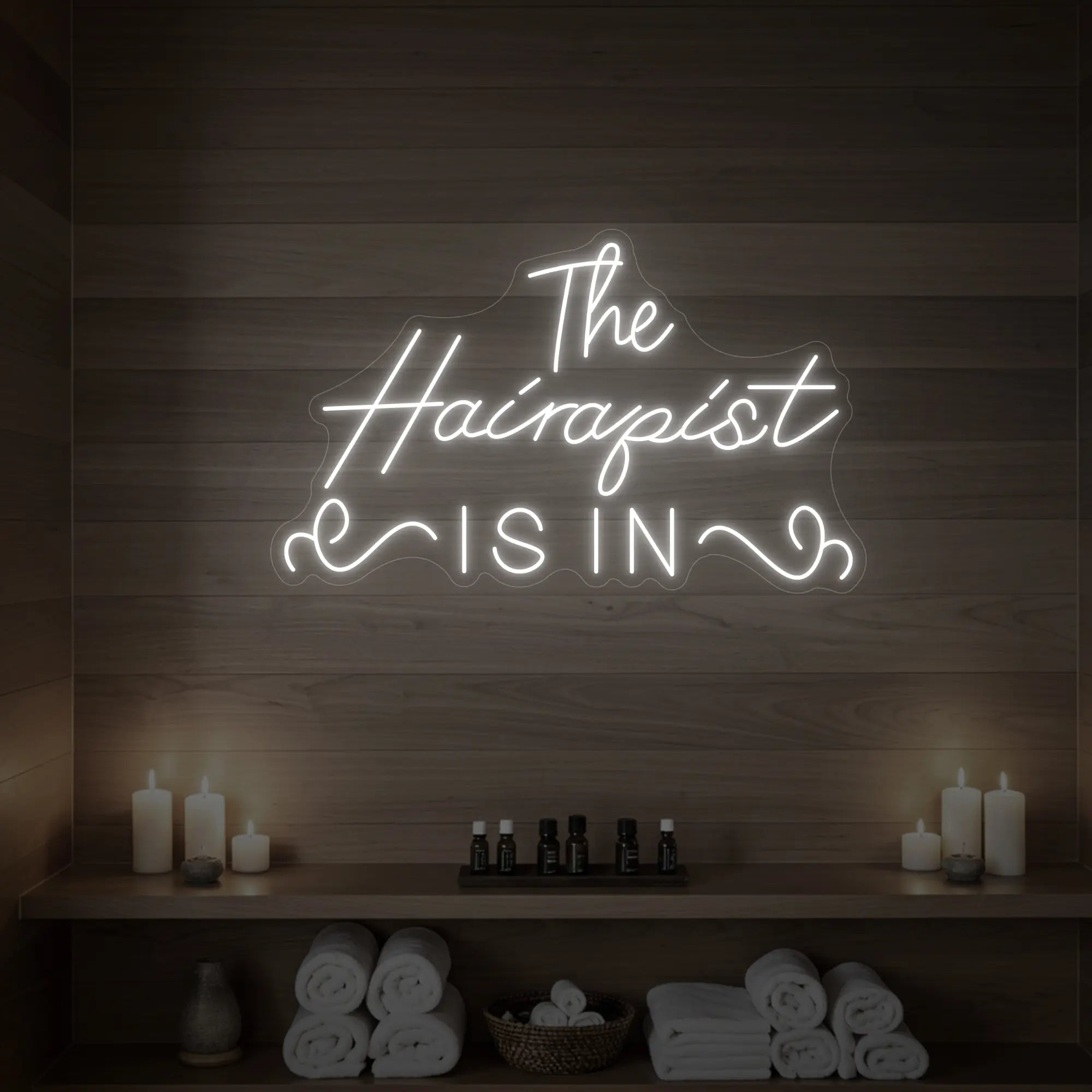 Photo of the 'The Hairapist Is In' neon sign glowing in cool white against a styled interior wall.