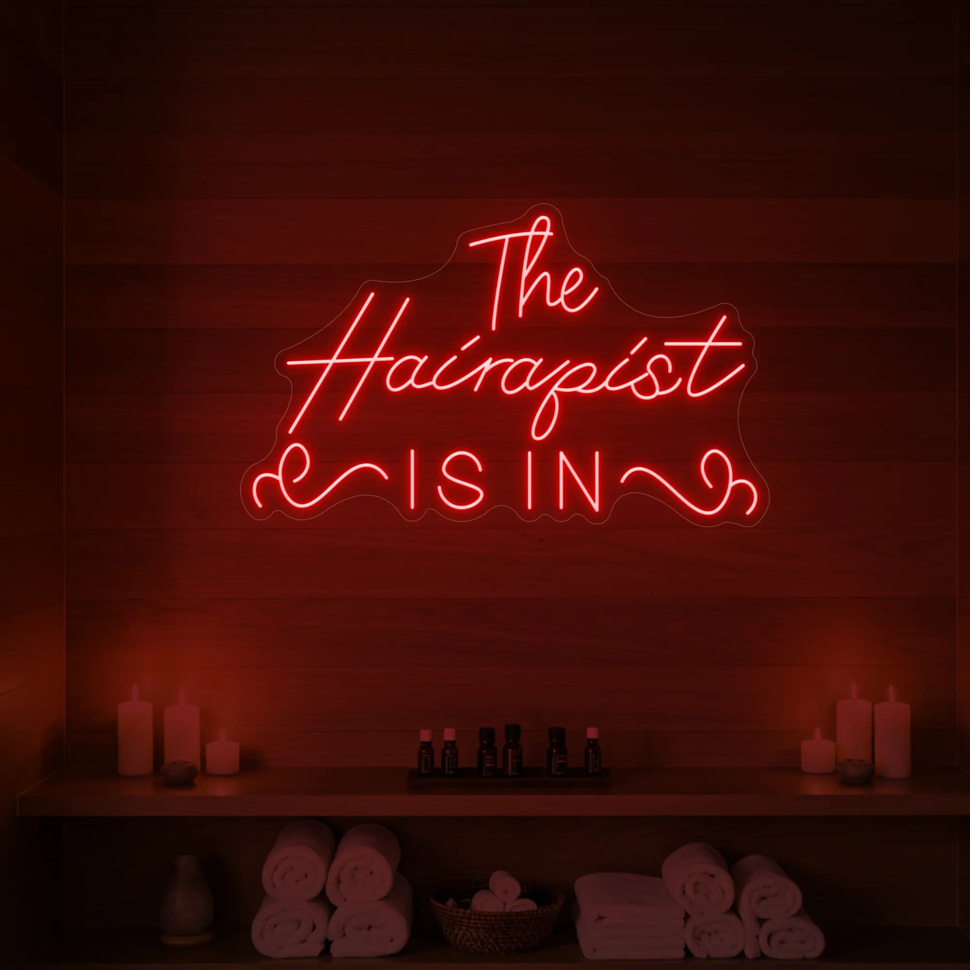 Photo of the 'The Hairapist Is In' neon sign glowing in red against a styled interior wall.