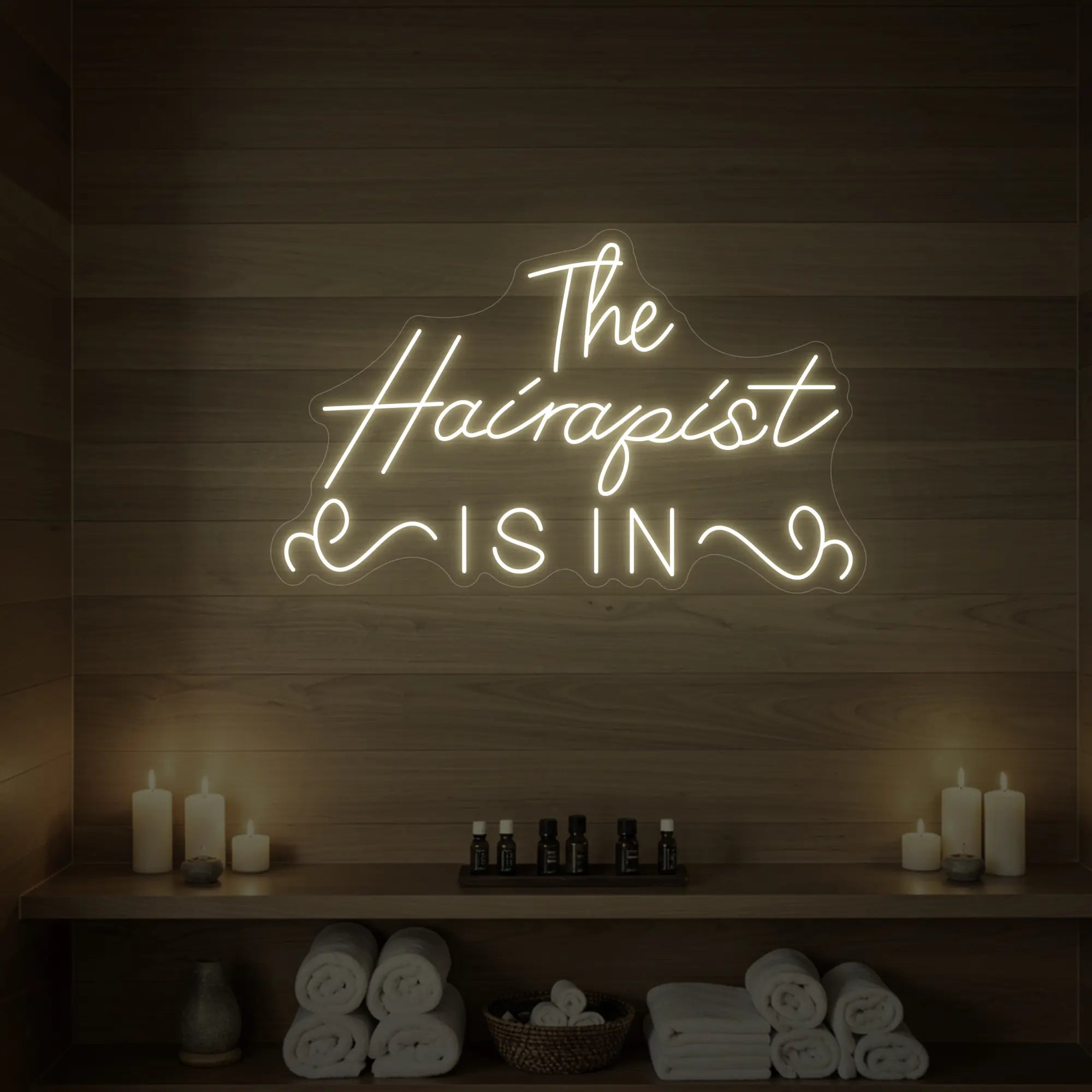 Photo of the 'The Hairapist Is In' neon sign glowing in warm white against a styled interior wall.