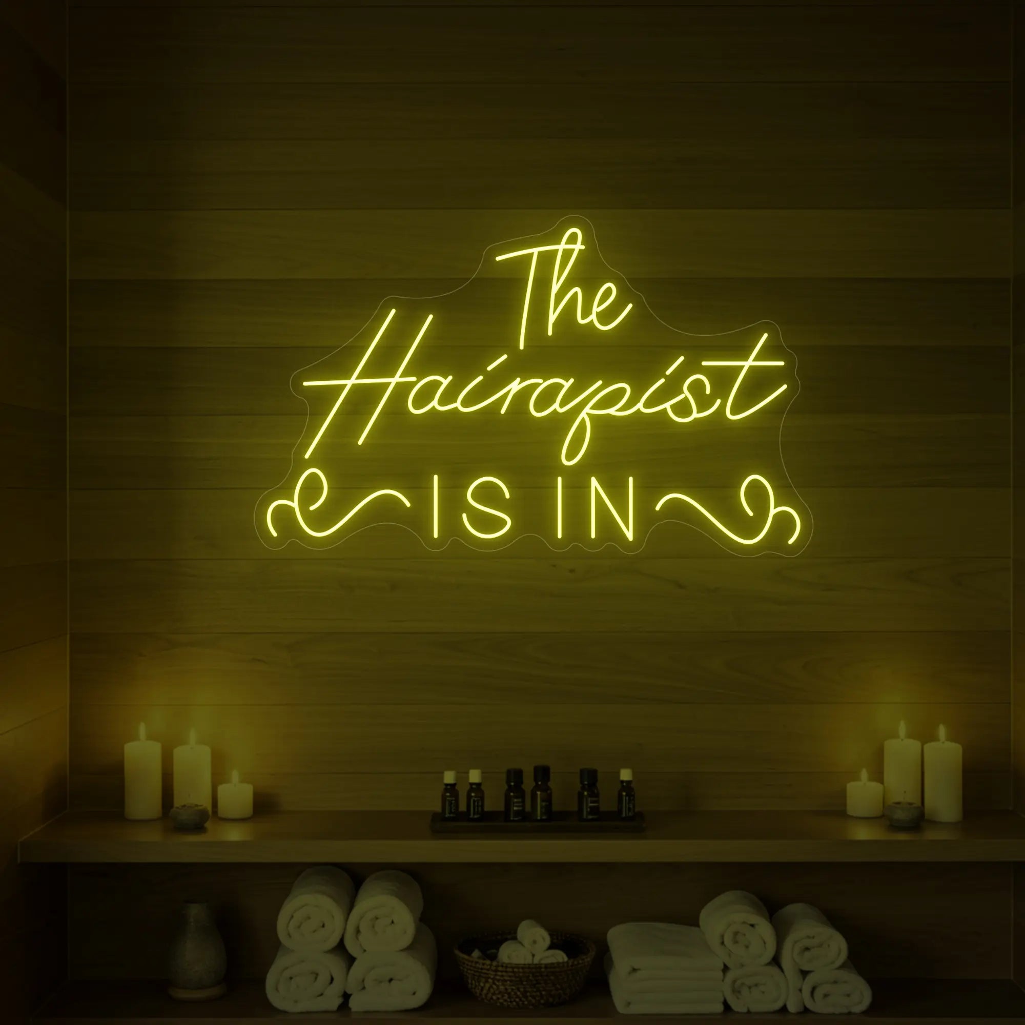 Photo of the 'The Hairapist Is In' neon sign glowing in lemon yellow against a styled interior wall.