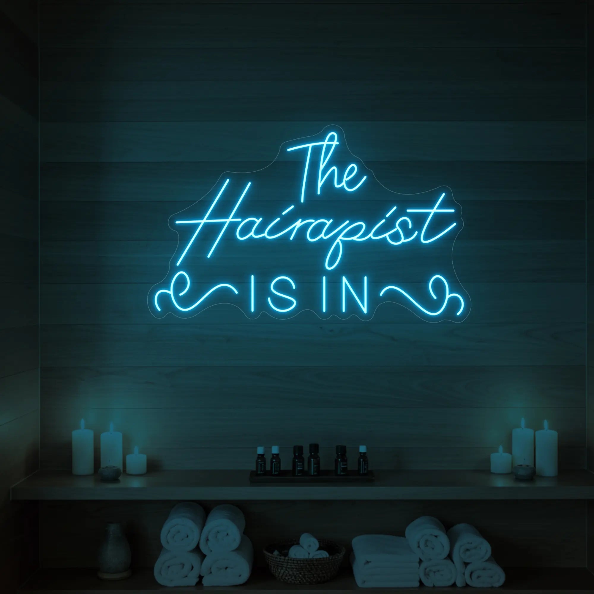 Photo of the 'The Hairapist Is In' neon sign glowing in ice blue against a styled interior wall.