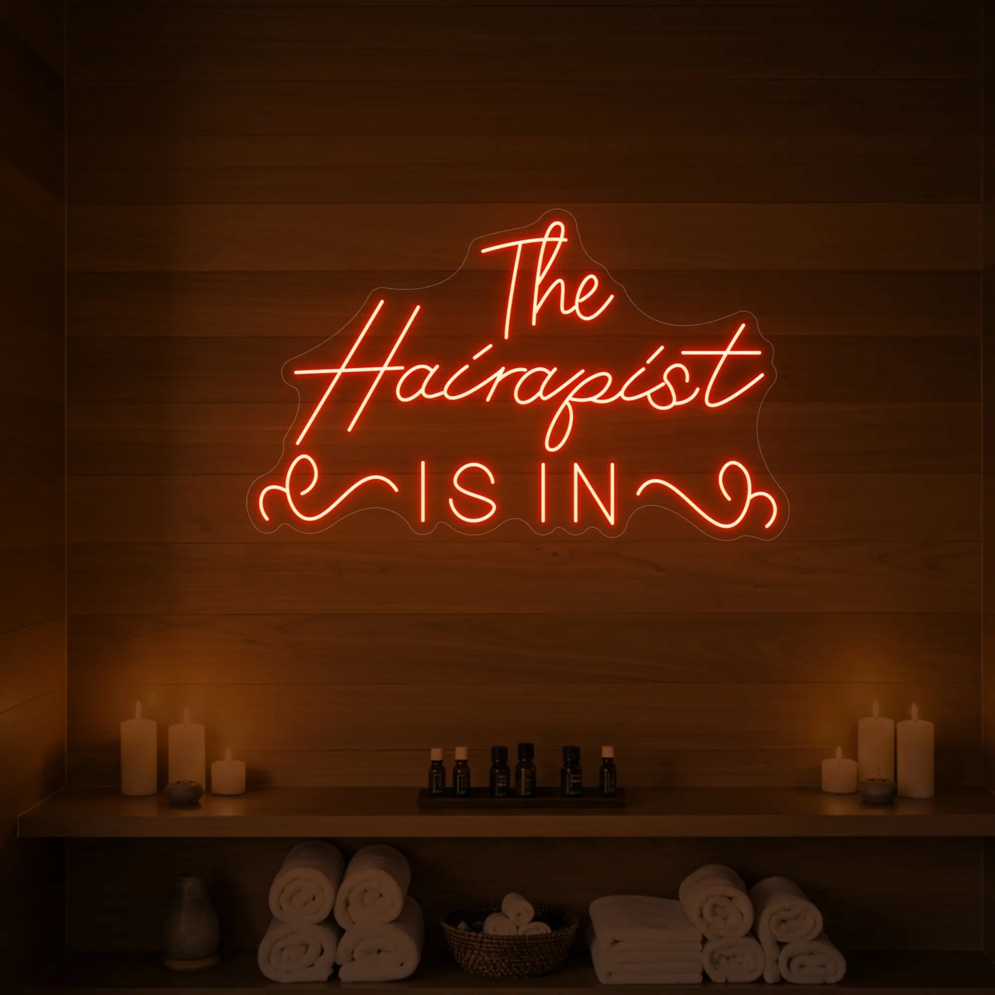 Photo of the 'The Hairapist Is In' neon sign glowing in golden yellow against a styled interior wall.