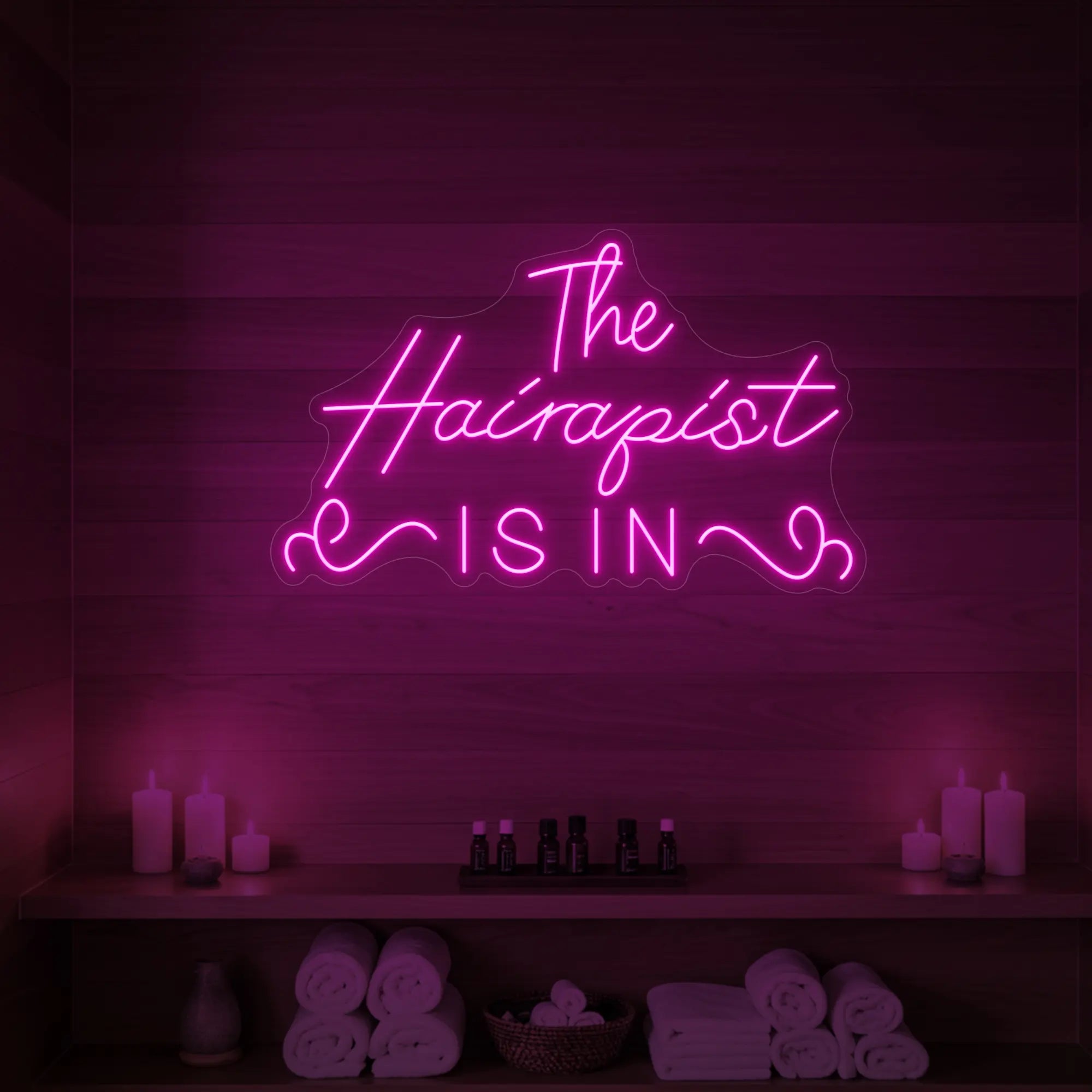 Photo of the 'The Hairapist Is In' neon sign glowing in light pink against a styled interior wall.