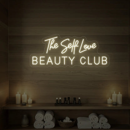 Photo of the 'The Self Love Beauty Club' neon sign glowing in warm white against a styled interior wall.