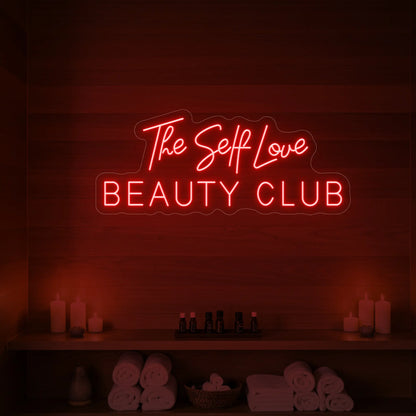 Photo of the 'The Self Love Beauty Club' neon sign glowing in red against a styled interior wall.