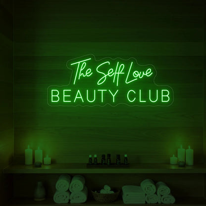 Photo of the 'The Self Love Beauty Club' neon sign glowing in green against a styled interior wall.