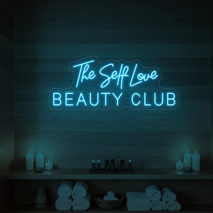 Photo of the 'The Self Love Beauty Club' neon sign glowing in ice blue against a styled interior wall.