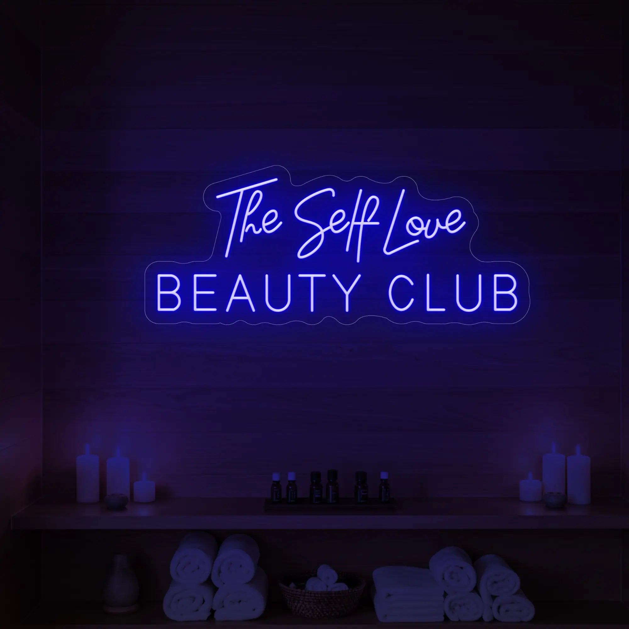 Photo of the 'The Self Love Beauty Club' neon sign glowing in green against a styled interior wall.