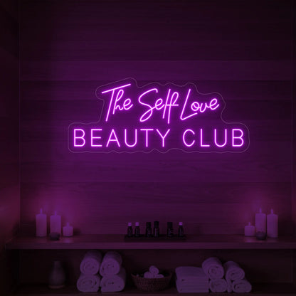 Photo of the 'The Self Love Beauty Club' neon sign glowing in deep pink against a styled interior wall.