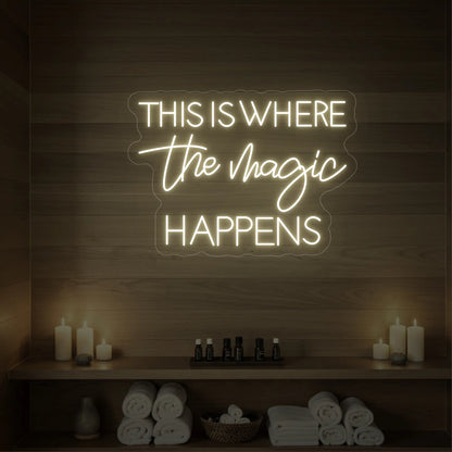 Photo of the 'This Is Where The Magic Happens' neon sign glowing in cool white against a wooden spa wall.