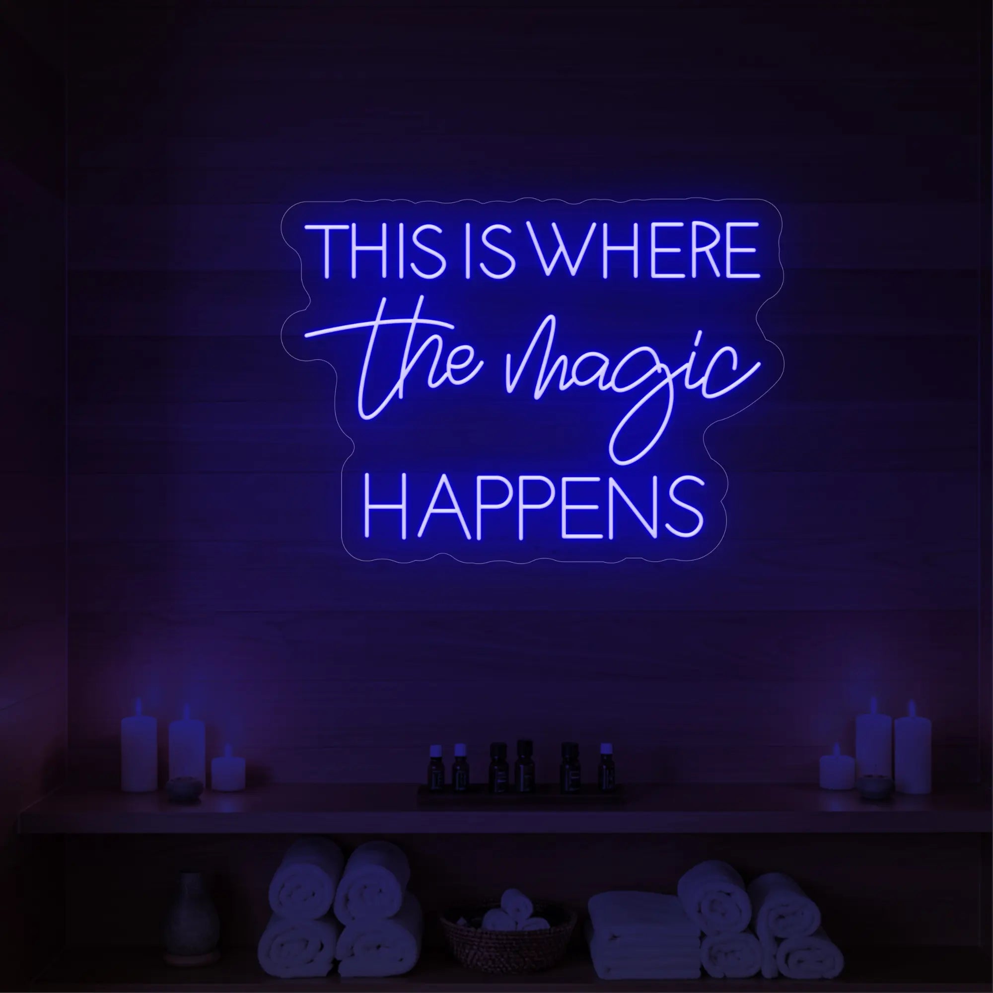 Photo of the 'This Is Where The Magic Happens' neon sign glowing in deep blue against a styled interior wall.