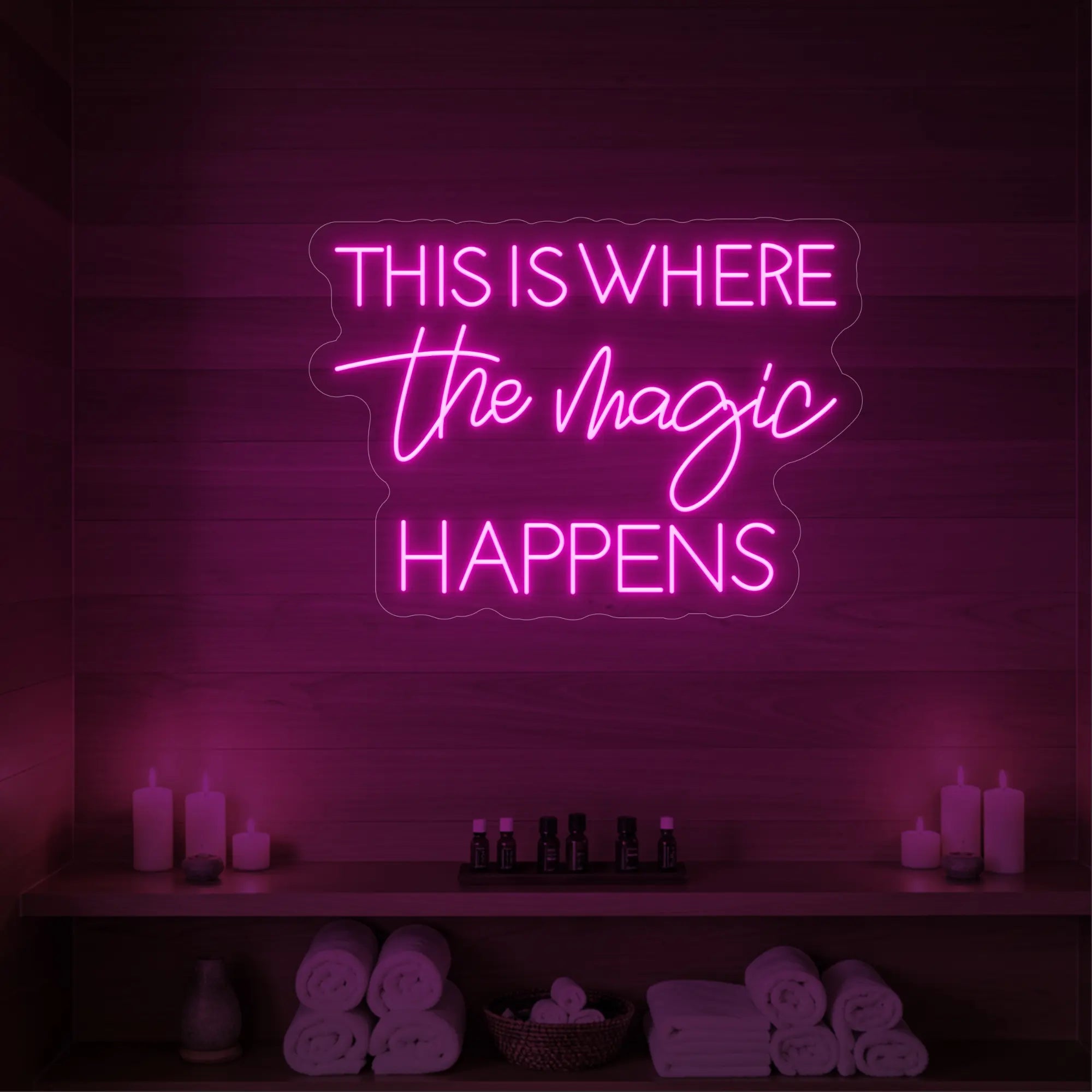 Photo of the 'This Is Where The Magic Happens' neon sign glowing in light pink against a styled interior wall.