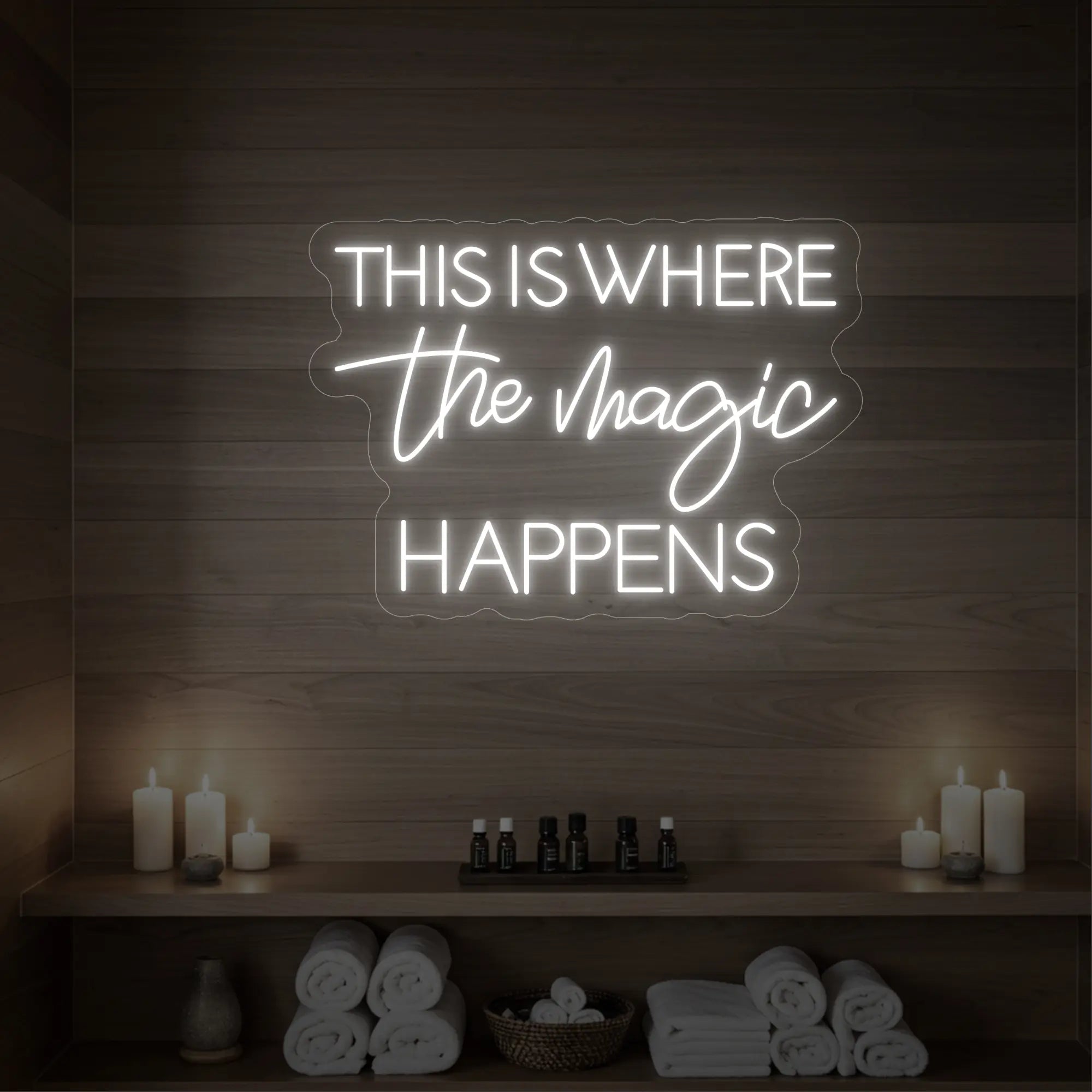 Photo of the 'This Is Where The Magic Happens' neon sign glowing in warm white against a wooden spa wall.