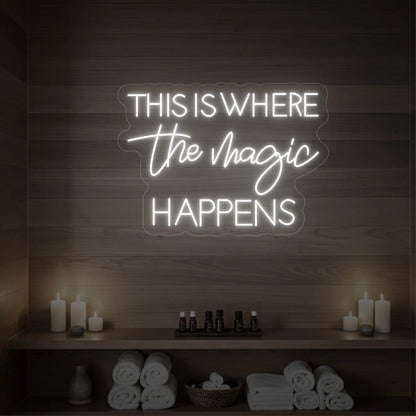 Photo of the 'This Is Where The Magic Happens' neon sign glowing in warm white against a wooden spa wall.