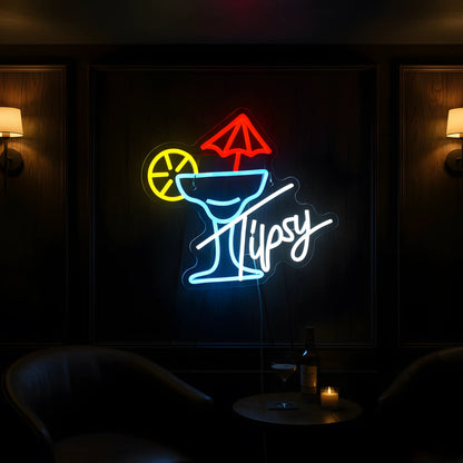 Photo of the 'Tipsy Cocktails' neon sign glowing in multi-color against a stylish cocktail bar-inspired wall.