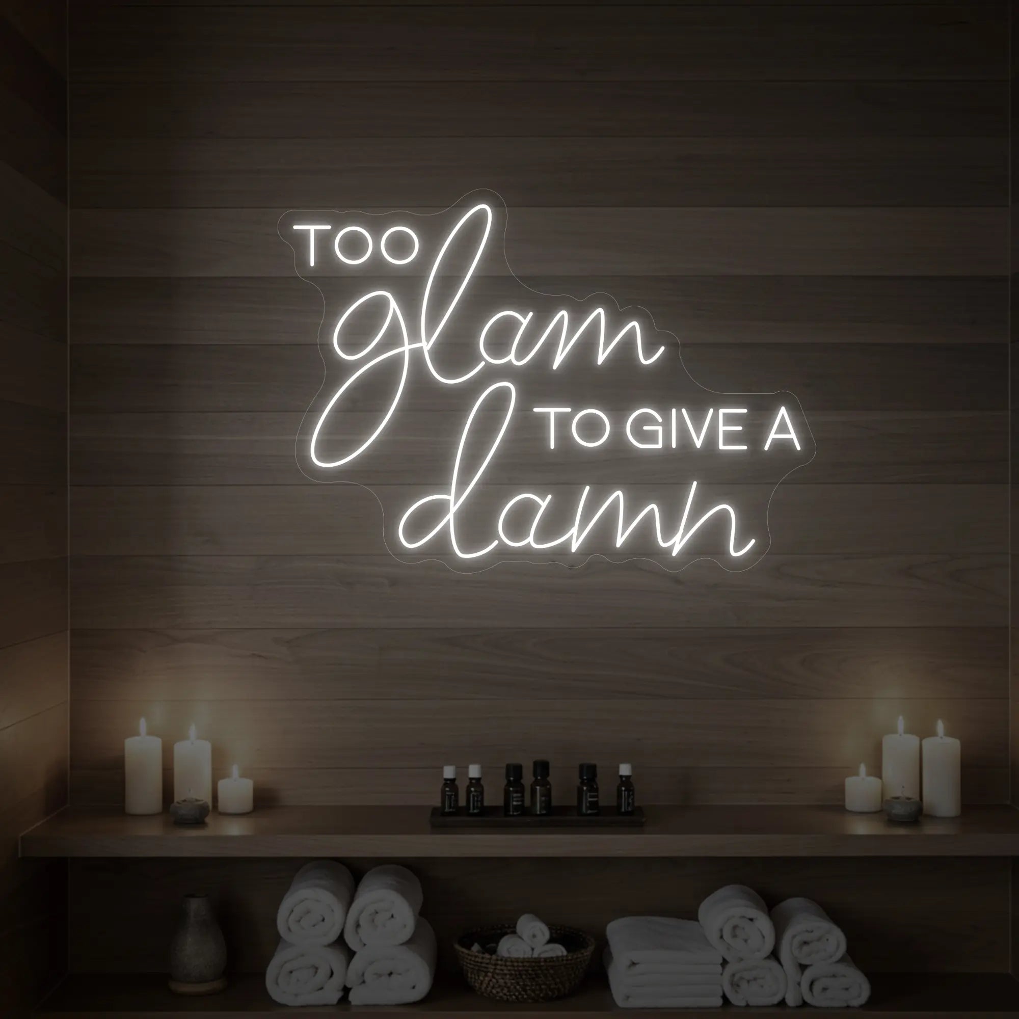 Photo of the 'TOO GLAM TO GIVE A DAMN' neon sign glowing in cool white against a styled interior wall.