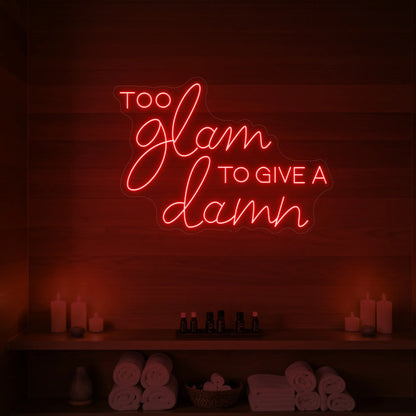 Photo of the 'TOO GLAM TO GIVE A DAMN' neon sign glowing in red against a styled interior wall.