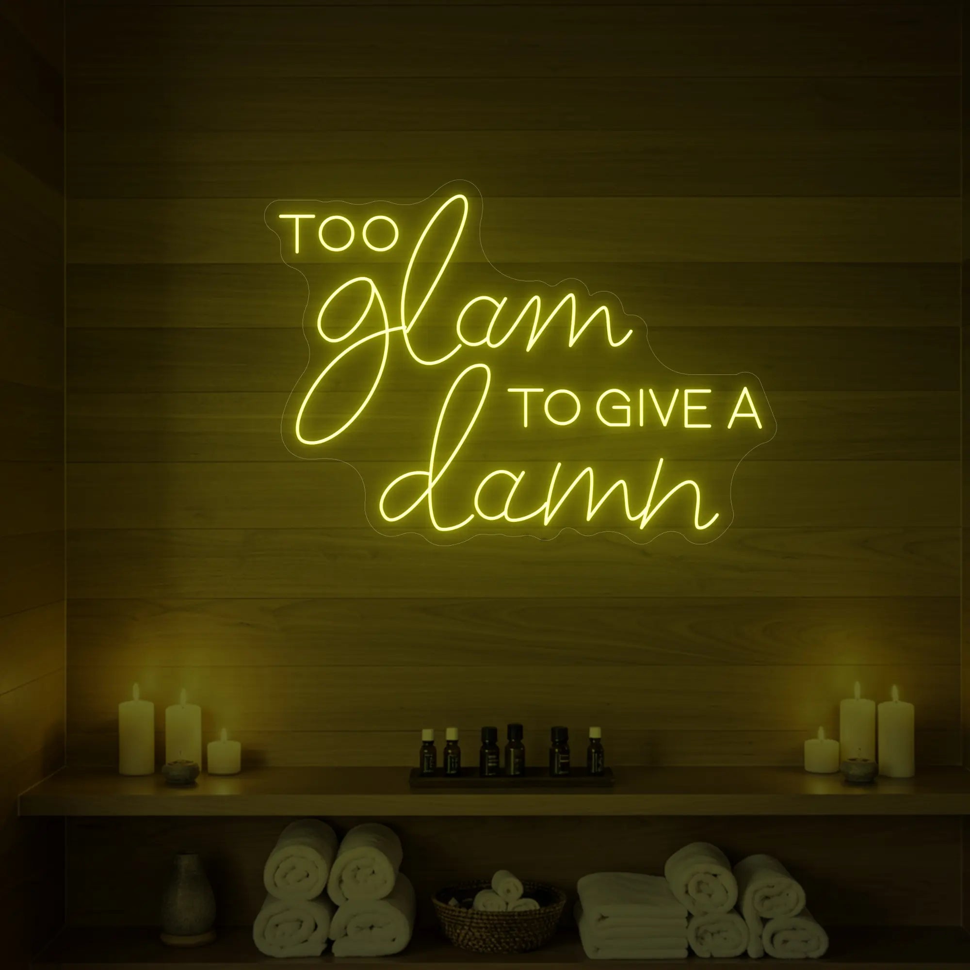 Photo of the 'TOO GLAM TO GIVE A DAMN' neon sign glowing in lemon yellow against a styled interior wall.