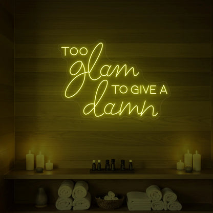 Photo of the 'TOO GLAM TO GIVE A DAMN' neon sign glowing in lemon yellow against a styled interior wall.