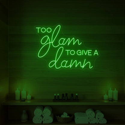 Photo of the 'TOO GLAM TO GIVE A DAMN' neon sign glowing in green against a styled interior wall.