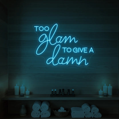 Photo of the 'TOO GLAM TO GIVE A DAMN' neon sign glowing in ice blue against a styled interior wall.