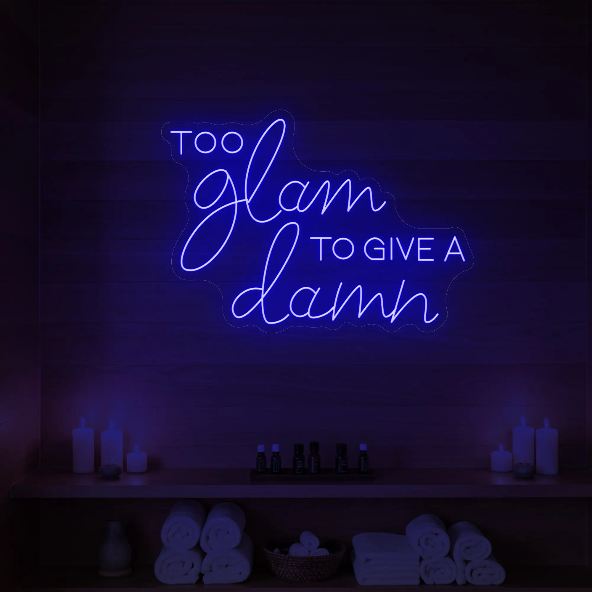 Photo of the 'TOO GLAM TO GIVE A DAMN' neon sign glowing in deep blue against a styled interior wall.