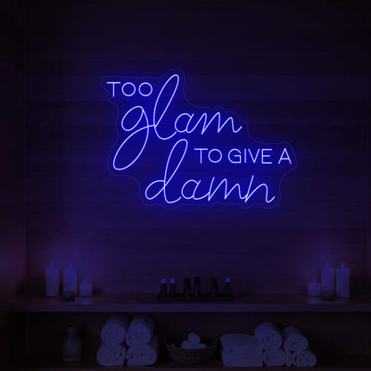 Photo of the 'TOO GLAM TO GIVE A DAMN' neon sign glowing in deep blue against a styled interior wall.