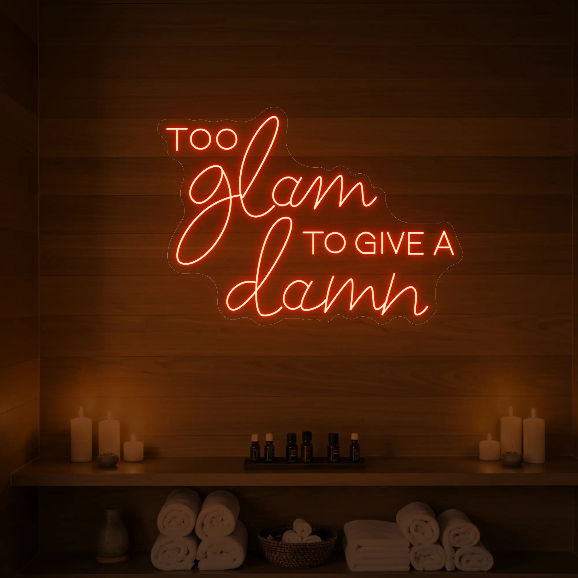 Photo of the 'TOO GLAM TO GIVE A DAMN' neon sign glowing in golden yellow against a styled interior wall.
