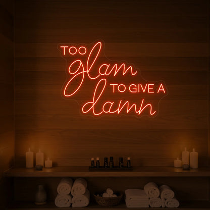 Photo of the 'TOO GLAM TO GIVE A DAMN' neon sign glowing in golden yellow against a styled interior wall.