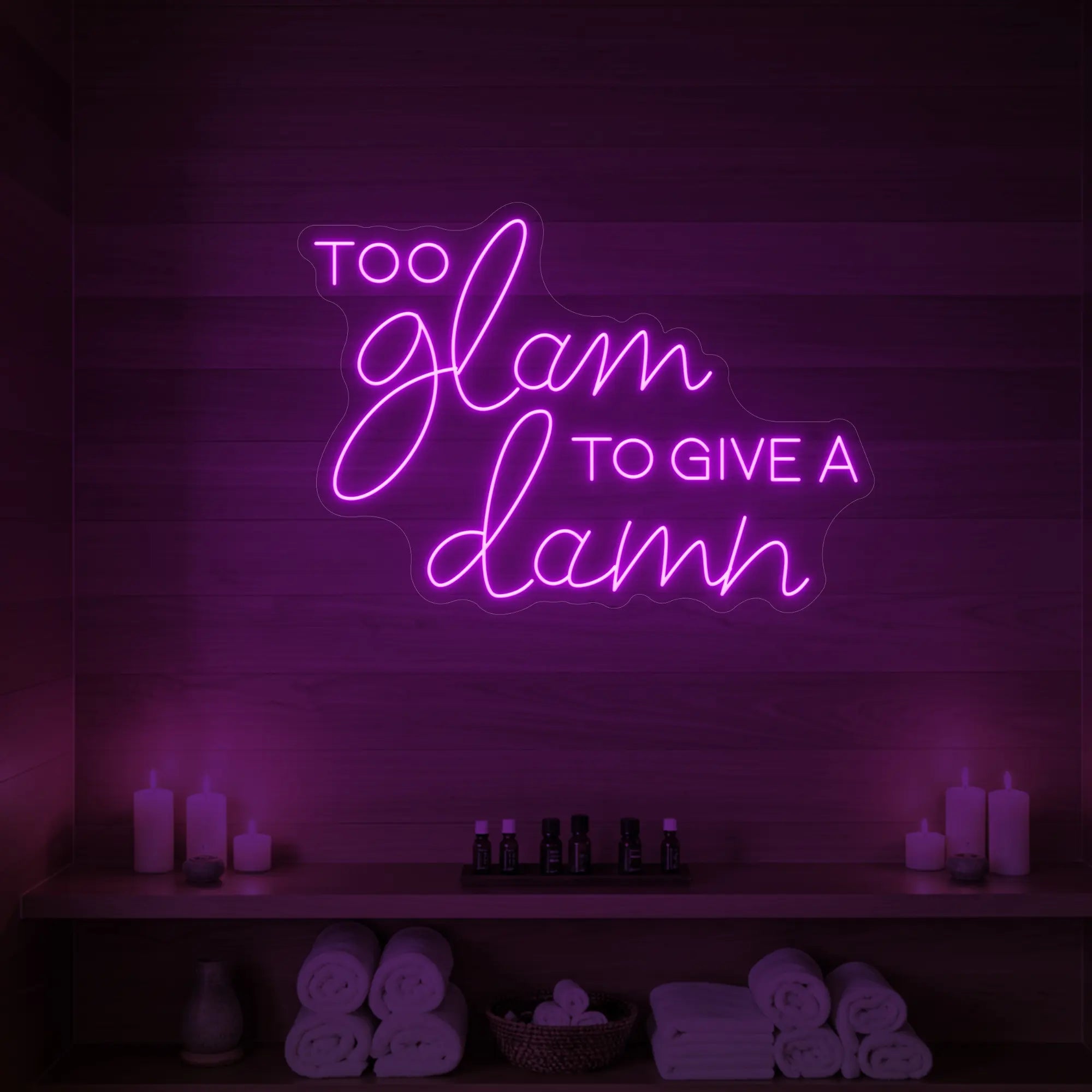 Photo of the 'TOO GLAM TO GIVE A DAMN' neon sign glowing in deep pink against a styled interior wall.