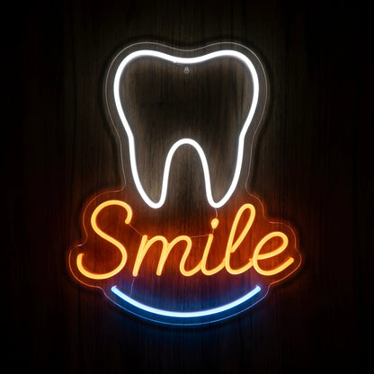 Tooth Smile Script LED neon sign featuring a glowing white tooth outline, orange cursive Smile lettering, and blue curved smile accent on clear acrylic backing against a dark wooden wall.