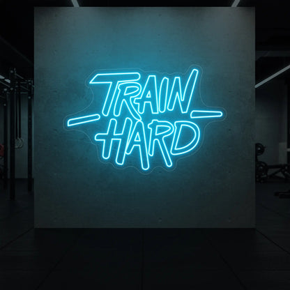 'TRAIN HARD' neon sign glowing in ice blue against a styled interior wall.