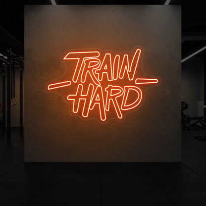  'TRAIN HARD' neon sign glowing in golden yellow against a styled interior wall.