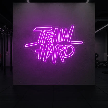'TRAIN HARD' neon sign glowing in dep pink against a styled interior wall.