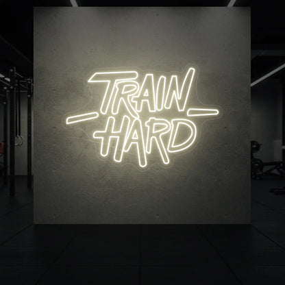  'TRAIN HARD' neon sign glowing in warm white against a styled interior wall.