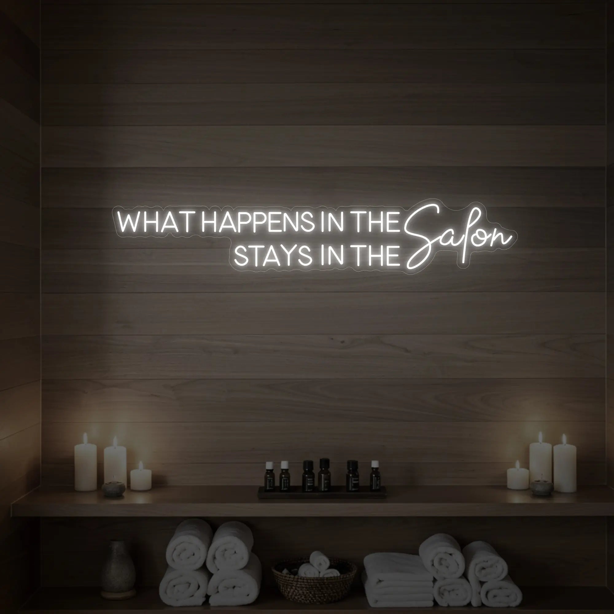 Photo of the 'WHAT HAPPENS IN THE SALON STAYS IN THE SALON' neon sign glowing in cool white against a styled interior wall.