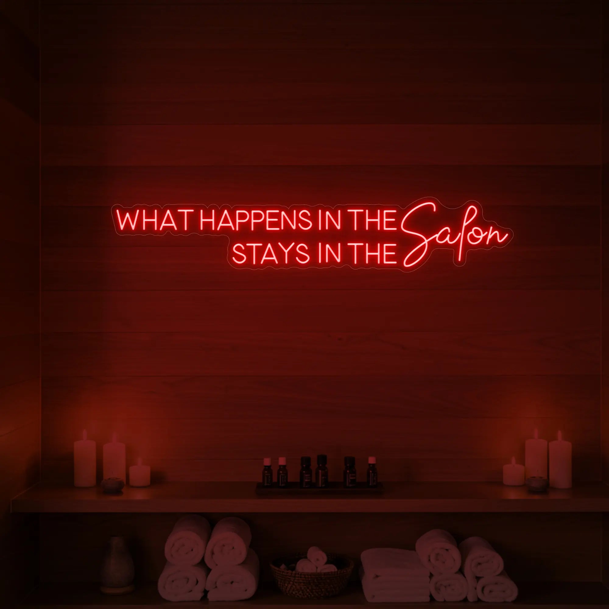 Photo of the 'WHAT HAPPENS IN THE SALON STAYS IN THE SALON' neon sign glowing in red against a styled interior wall.