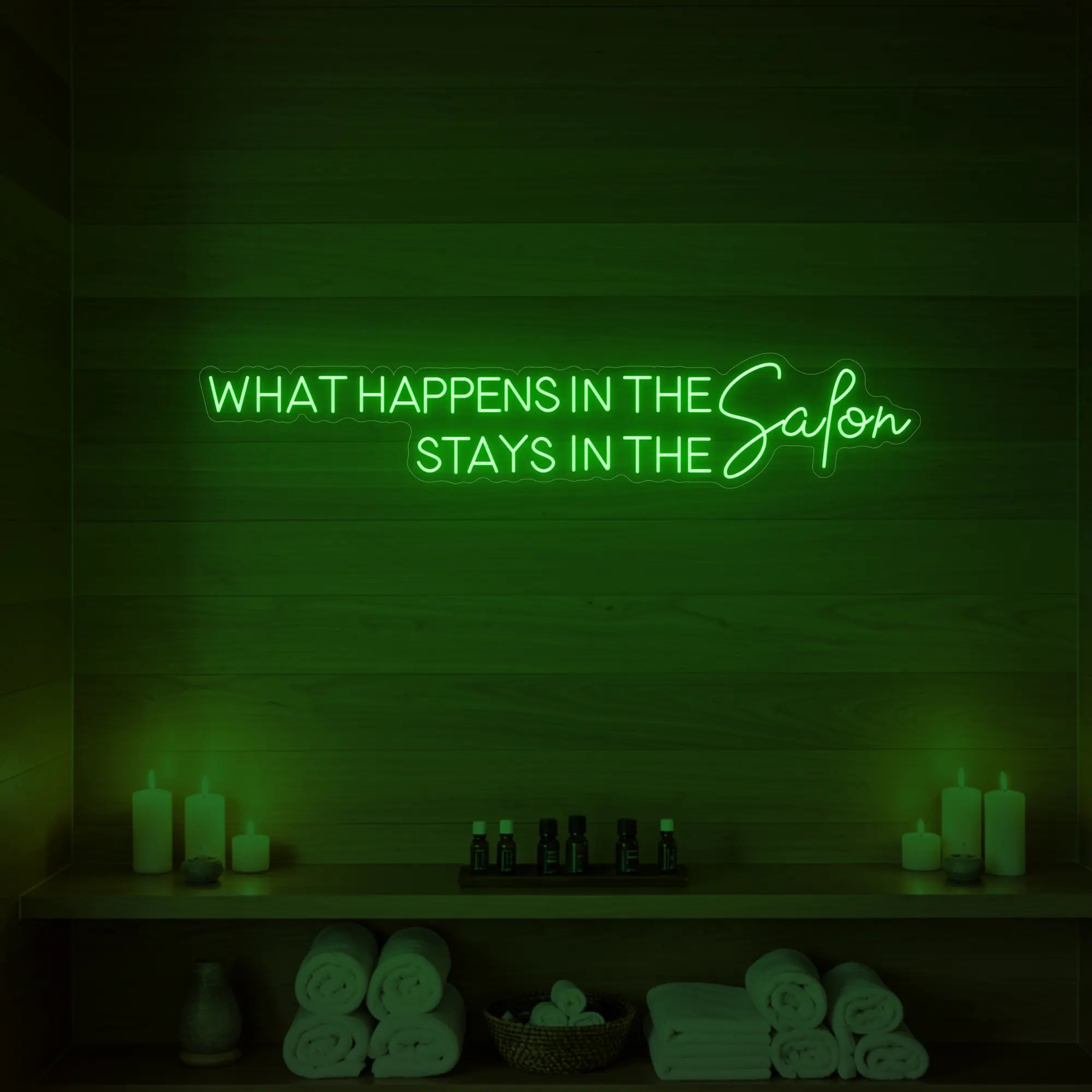 Photo of the 'WHAT HAPPENS IN THE SALON STAYS IN THE SALON' neon sign glowing in green against a styled interior wall.