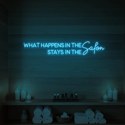 Photo of the 'WHAT HAPPENS IN THE SALON STAYS IN THE SALON' neon sign glowing in ice blue against a styled interior wall.