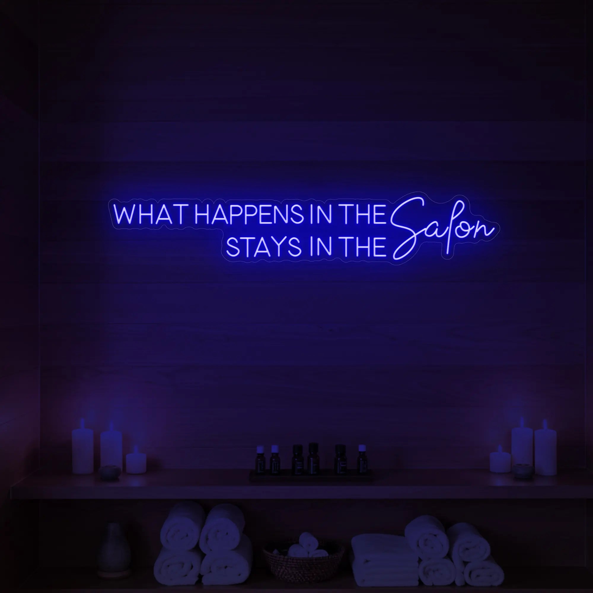 Photo of the 'WHAT HAPPENS IN THE SALON STAYS IN THE SALON' neon sign glowing in deep blue against a styled interior wall.