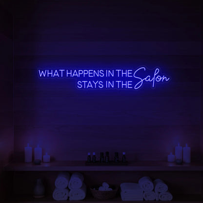 Photo of the 'WHAT HAPPENS IN THE SALON STAYS IN THE SALON' neon sign glowing in deep blue against a styled interior wall.