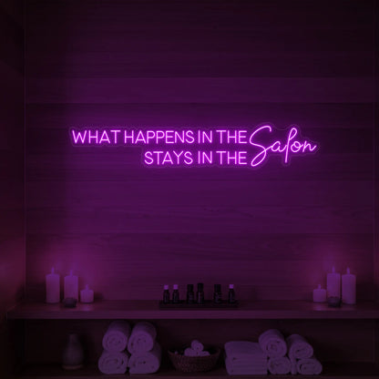 Photo of the 'WHAT HAPPENS IN THE SALON STAYS IN THE SALON' neon sign glowing in deep pink against a styled interior wall.