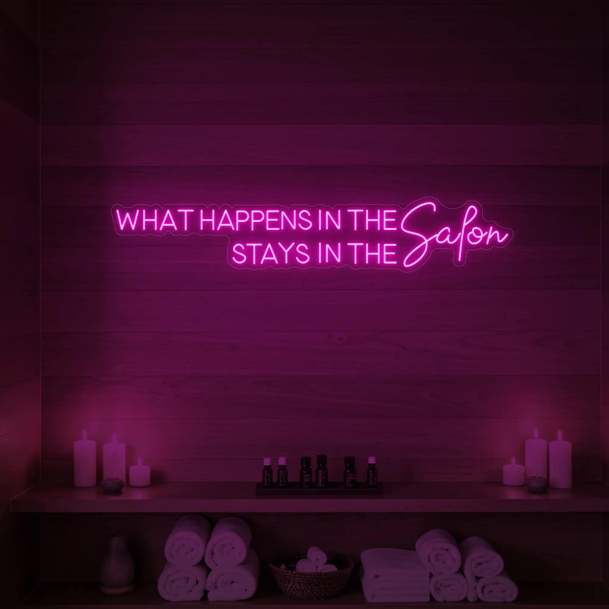 Photo of the 'WHAT HAPPENS IN THE SALON STAYS IN THE SALON' neon sign glowing in light pink against a styled interior wall.