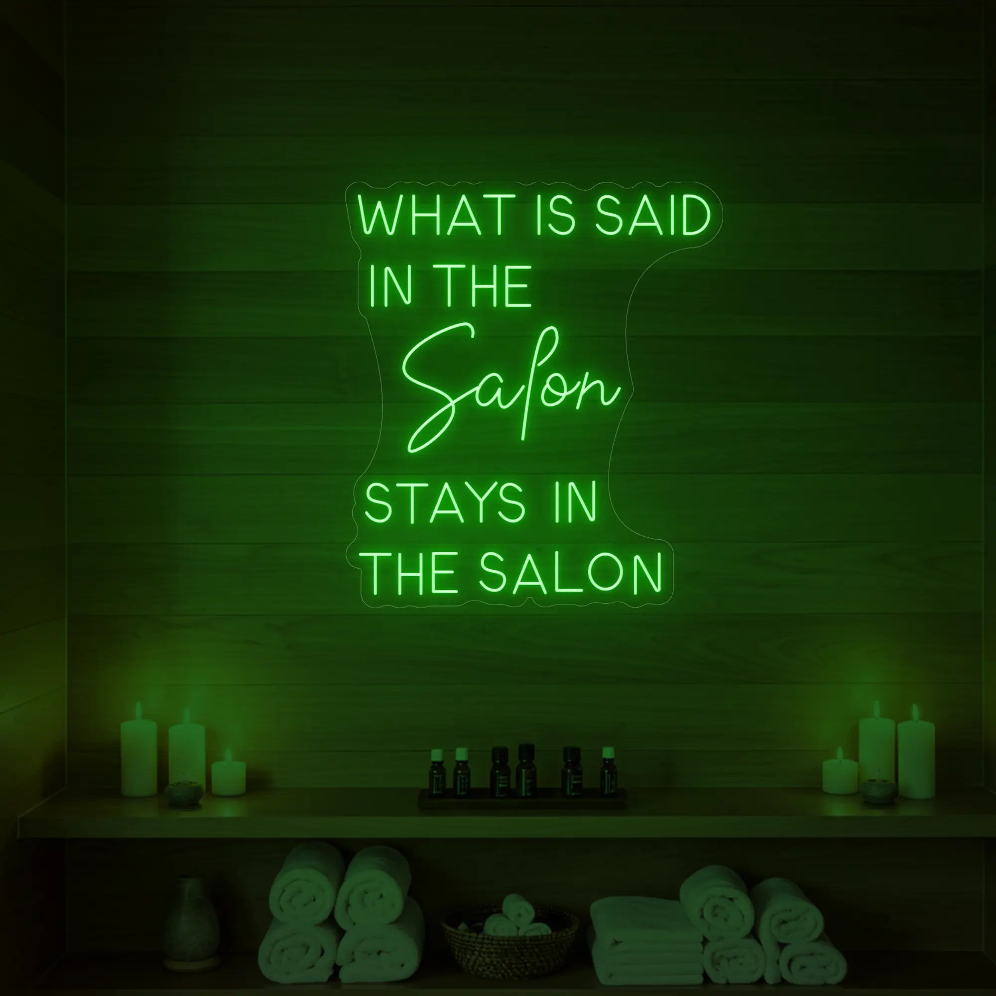 Photo of the 'What is Said in the Salon Stays in the Salon' neon sign glowing in green against a styled interior wall.