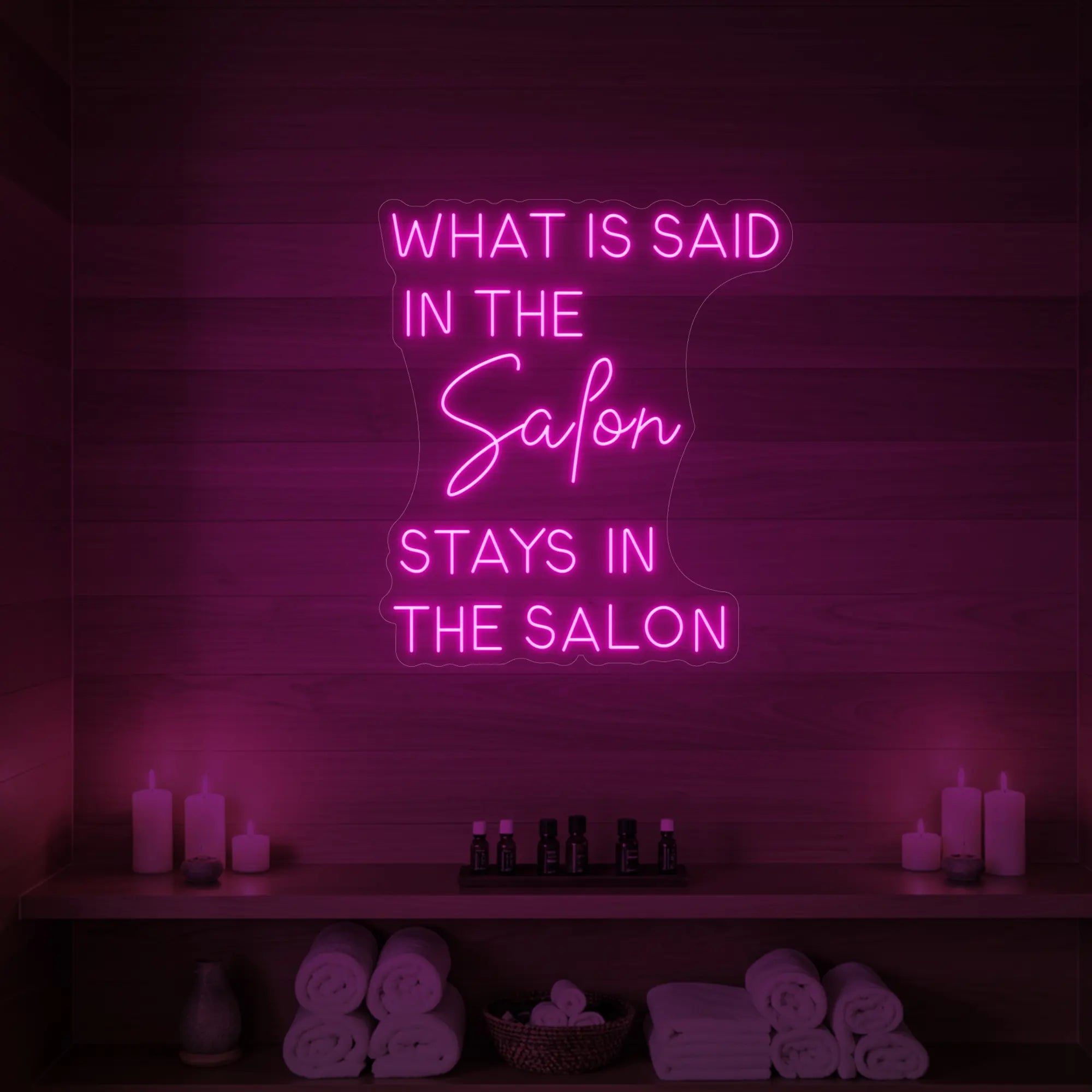 Photo of the 'What is Said in the Salon Stays in the Salon' neon sign glowing in light pink against a styled interior wall.