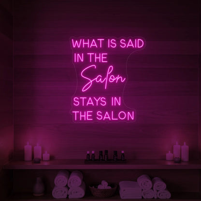 Photo of the 'What is Said in the Salon Stays in the Salon' neon sign glowing in light pink against a styled interior wall.
