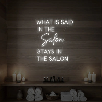 Photo of the 'What is Said in the Salon Stays in the Salon' neon sign glowing in cool white against a styled interior wall.