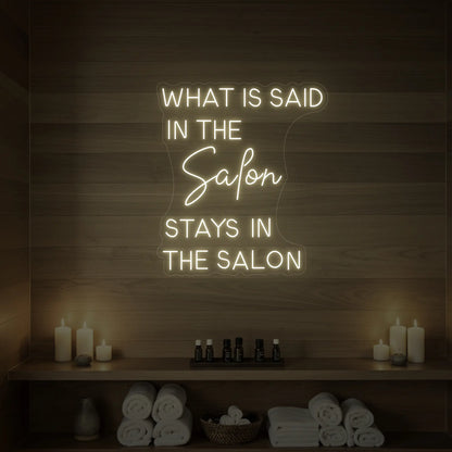 Photo of the 'What is Said in the Salon Stays in the Salon' neon sign glowing in warm white against a styled interior wall.