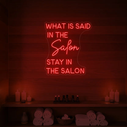 Photo of the 'WHAT IS SAID IN THE SALON STAY IN THE SALON' neon sign glowing in red against a styled interior wall.