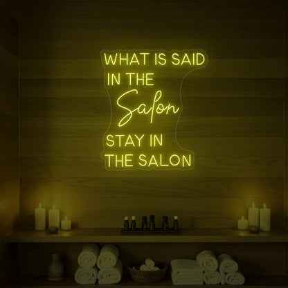 Photo of the 'WHAT IS SAID IN THE SALON STAY IN THE SALON' neon sign glowing in lemon yellow against a styled interior wall.